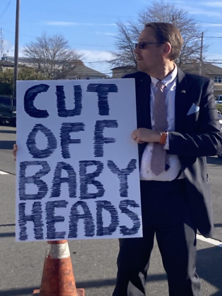 man holding protest sign that reads, "cut off baby heads"