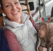 woman with big smile and kind eyes with pink long sleeve shirt and a white puff jacket holding a baby who is looking at her adoringly